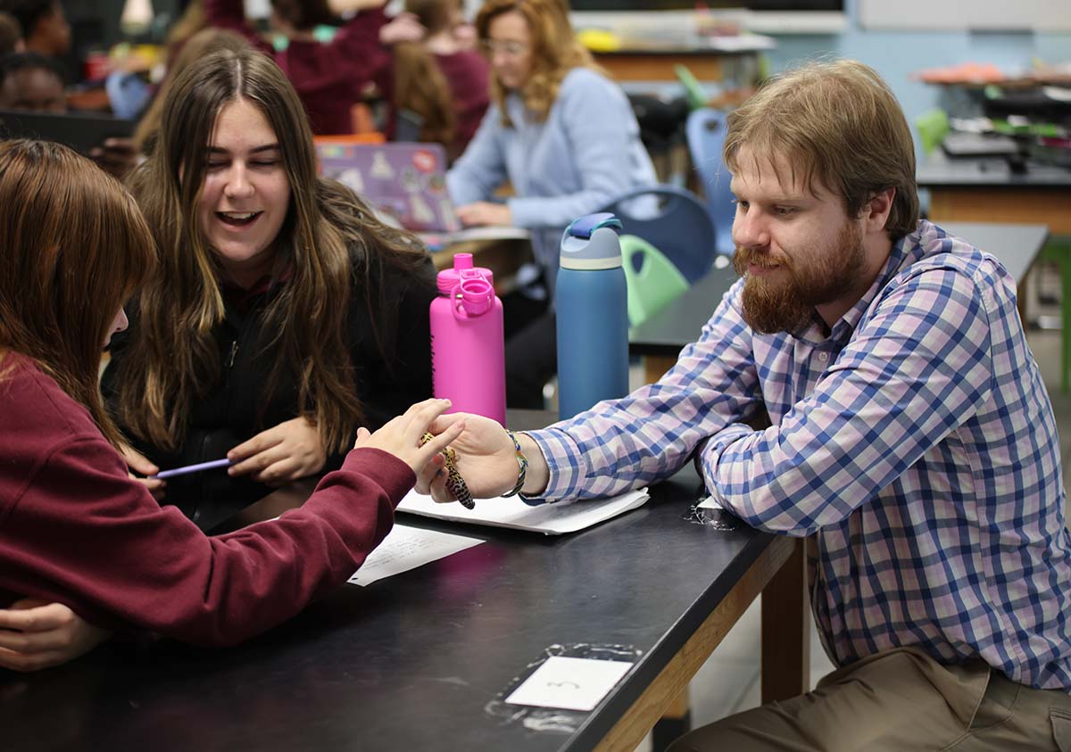 HSA Teacher smiles while kneeling beside a young student in a classroom setting.